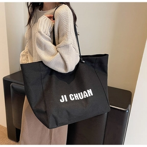 Detail view of a large black canvas tote bag with white JI CHUAN text on a model