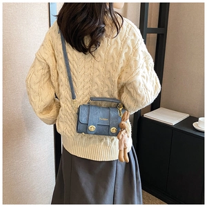 Blue textured mini crossbody bag with gold clasps and cute rabbit charm on a beige sweater
