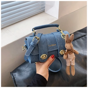 Close-up of blue denim handbag with gold locks and a cute brown knitted rabbit charm
