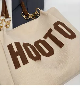Detail of off-white corduroy tote bag showing leather logo patch and metal chain strap