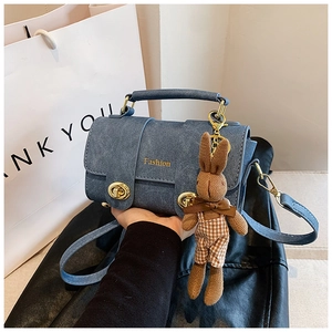 Macro detail of blue matte handbag with golden hardware and cute bunny pendant
