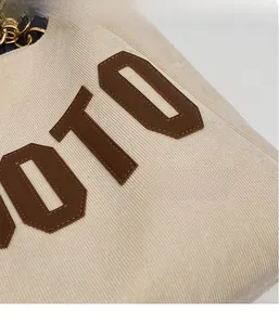 Close-up of beige corduroy tote bag featuring brown leather letter patch and chain strap