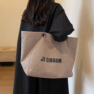 Large beige woven canvas tote bag with black straps worn by model for daily commuting