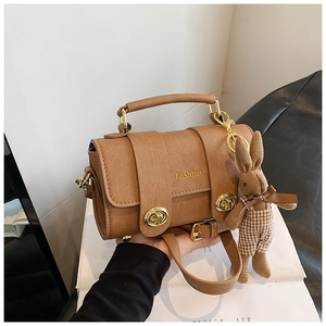 Detail of brown PU leather bag featuring gold Fashion logo and cute rabbit charm