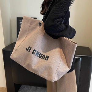 Large beige canvas tote bag with black lettering and durable shoulder strap for women