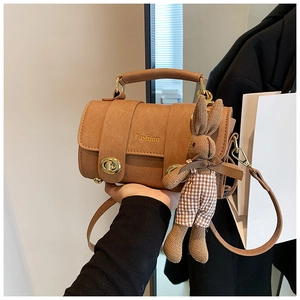 Detail of brown suede cylinder bag with gold turn-lock and cute bunny charm accessory