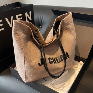 Minimalist beige woven tote bag with black leather straps shown in a luxury gift box