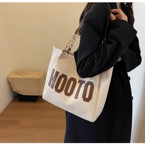 Detail of off-white canvas tote bag with brown leather HOOTO patch and chain strap