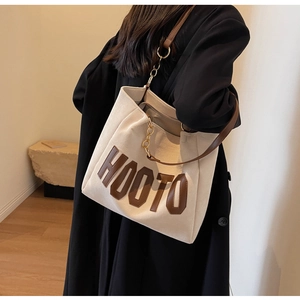 Detail shot of beige canvas tote bag with brown leather straps and HOOTO logo