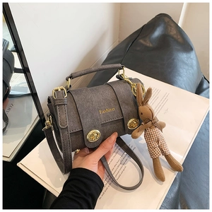 Detail of dark grey textured cylindrical bag with gold buckles and plush rabbit charm