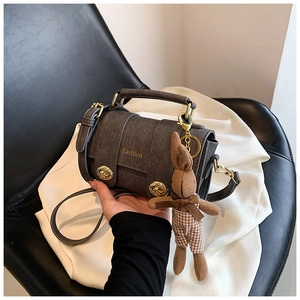 Macro shot of dark grey cylinder bag featuring golden clasp and fashion text detail