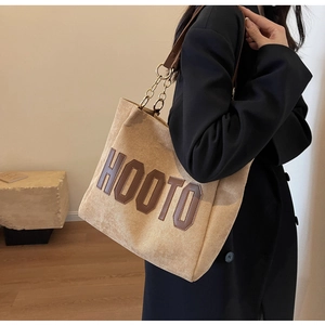 Detail of beige corduroy tote with brown leather lettering and chain strap on shoulder