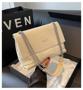 Detailed view of cream quilted shoulder bag with metal logo and silver chain strap
