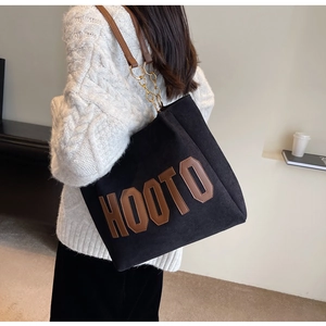 Detailed texture of black corduroy tote bag with brown leather letters and chain handle