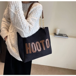 Detail of a large black tote bag with HOOTO leather patch and metal chain strap