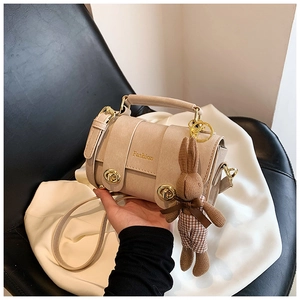 Detail of cream cylindrical crossbody bag with gold Fashion text and rabbit charm