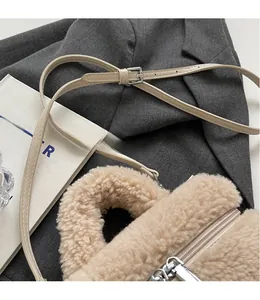 Détail d'un sac seau en peluche beige avec bandoulière en cuir sur fond de costume chic