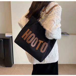 Detail of black canvas tote bag with brown HOOTO letters and chain strap on shoulder
