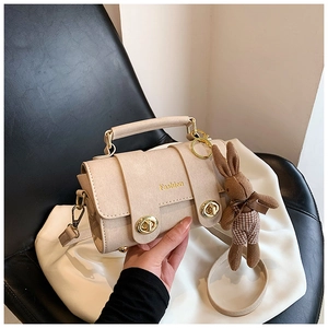 Close-up of beige crossbody square bag with gold clasps and plush bunny keychain