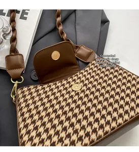 Detail of houndstooth underarm bag featuring a brown leather strap and hidden magnetic buckle
