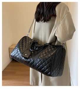 Detail of a large black quilted leather duffel bag styled with a modern trench coat