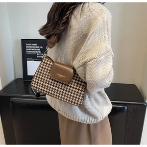 Detail of houndstooth fabric texture and brown leather strap on elegant underarm bag
