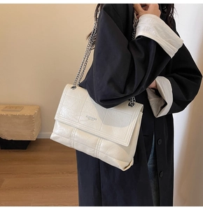 Detail of off-white quilted crossbody bag with silver chain strap on model shoulder