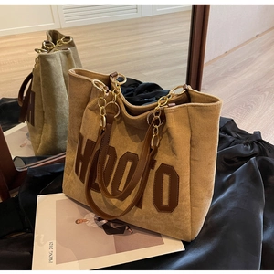 Detail of corduroy tote bag with HODTO patch, brown leather handles and gold chain accents