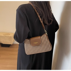 Detail of retro houndstooth underarm bag with brown leather flap and woven strap