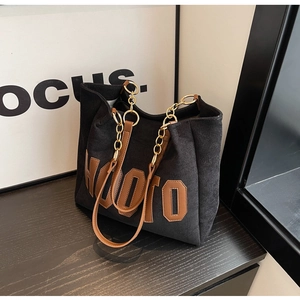 Macro detail of black corduroy tote bag with chain strap and leather letter patch