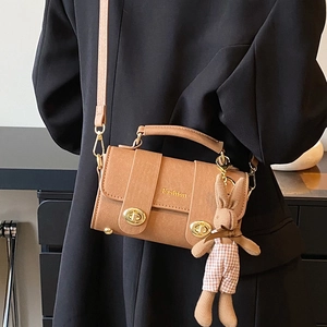Brown leather crossbody square bag with gold buckle and rabbit pendant on black blazer
