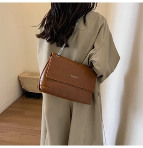 Detail of a brown quilted leather crossbody bag with silver chain strap and flap closure