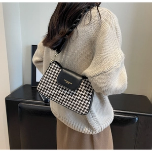 Detail view of houndstooth underarm bag with thick black chain strap on model