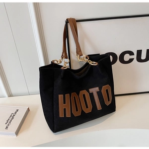 Detail of black corduroy tote bag featuring brown HOOTO applique and gold metal chain strap