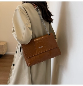Detail of a brown leather shoulder bag with chain strap worn over a khaki trench coat