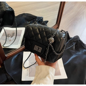 Detailed close-up of black quilted shoulder bag with silver ball chain strap and lock