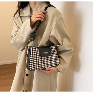 Detail of houndstooth underarm bag with leather flap and golden metal buckles