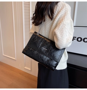 Close-up of black glossy wrinkled leather texture and silver chain strap on square bag
