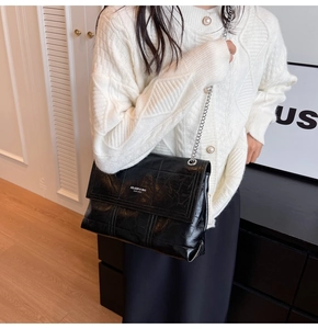 Detail of glossy black leather handbag with silver chain strap and refined stitching