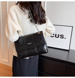 Detail of black leather crossbody bag with silver chain strap and quilted texture