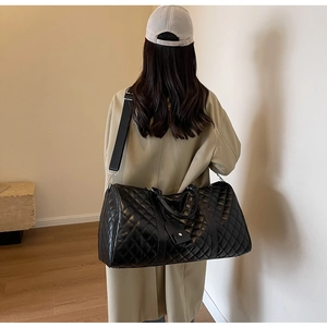 Detail of a large black quilted travel bag with adjustable strap and luggage tag