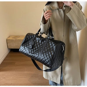 Quilted black travel bag with top handles and shoulder strap styled on a trench coat model