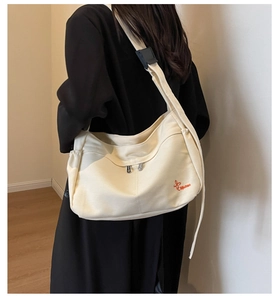 Detail of adjustable black strap and red embroidery on cream canvas tote bag