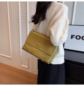 Detail of olive green pleated leather bag featuring silver chain strap on a model