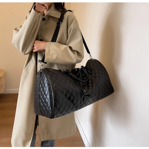 Detailed view of black quilted large travel bag with adjustable strap worn by model