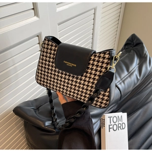 Detail of houndstooth crossbody bag with black leather flap and golden hardware