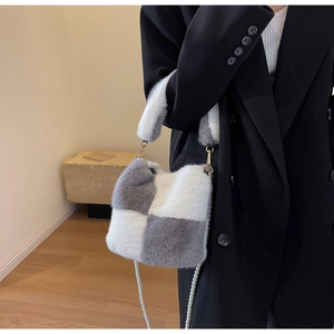 Detail of plush checkerboard bucket bag with pearl strap on model in black blazer