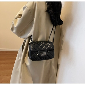 Detail of black quilted leather shoulder bag with silver metal turn-lock on beige coat
