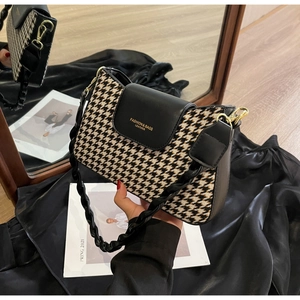 Detail of houndstooth shoulder bag with black leather flap and golden branding
