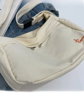 Close-up of cream canvas bag featuring orange dragonfly embroidery and a white nylon strap